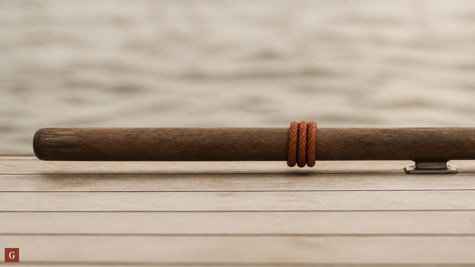 Barre franche en bois d'un voilier, posée sur un pont aux tons sable